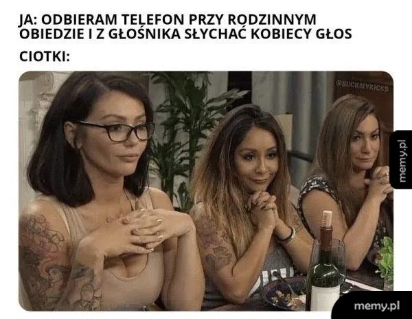 Trzy kobiety siedzą przy stole, jedna z nich trzyma ręce złożone na kolanach.