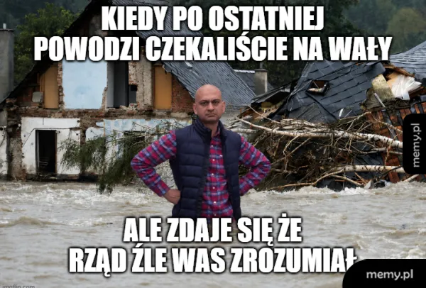 Mężczyzna w kamizelce stoi na tle zniszczonego budynku po powodzi.