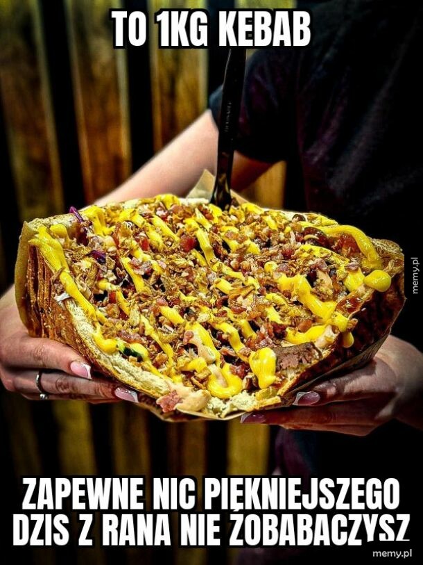 Osoba trzymająca olbrzymiego kebaba o wadze 1 kg polanego sosem.
