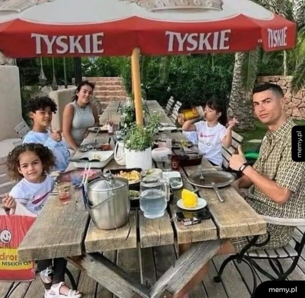 Cristiano Ronaldo z rodziną siedzi przy drewnianym stole pod parasolem z logo Tyskie.